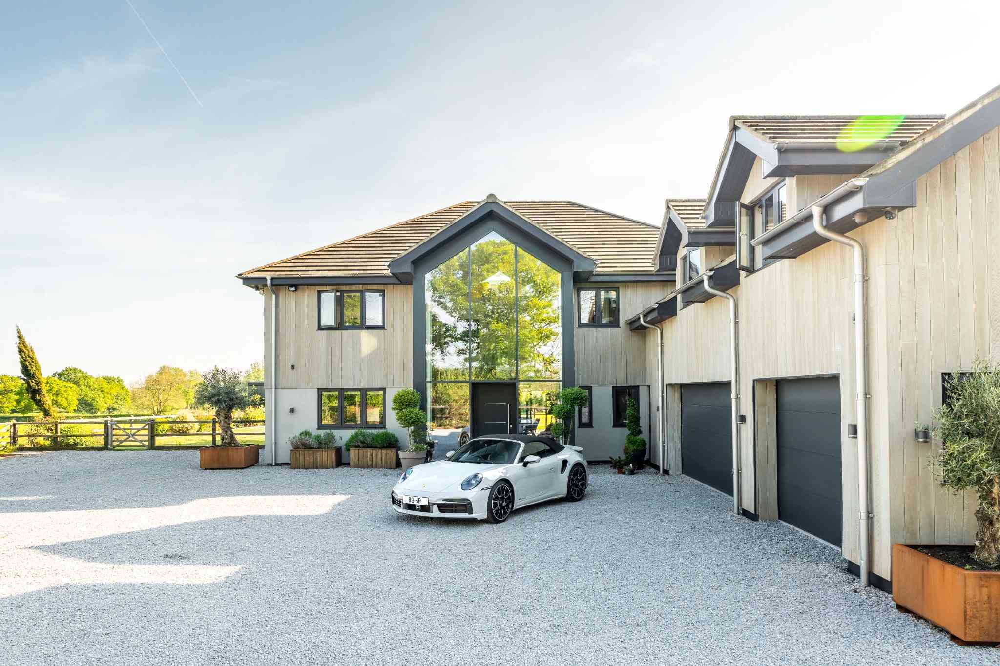 Luxury UK home with a double height glass entrance and a white Porsche on the gravel driveway, a prime property of the kind listed on Moveli